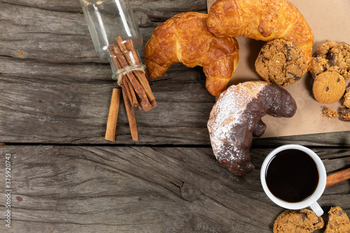 View of cookies, pretzels and croissants put on a table cloth with a cup of coffee on wooden surface