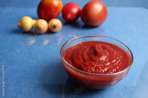 Wallpaper Mural red tomato sauce ketchup in a glass salad bowl a saucepan next to the back are vegetables red tomatoes and onions on a blue background copy space Torontodigital.ca