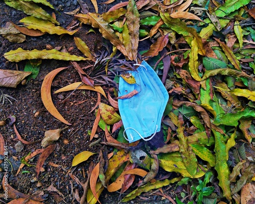 A Covid 19 mask lying on the road with waste leaves. It was thrown away by someone without properly disposing it.