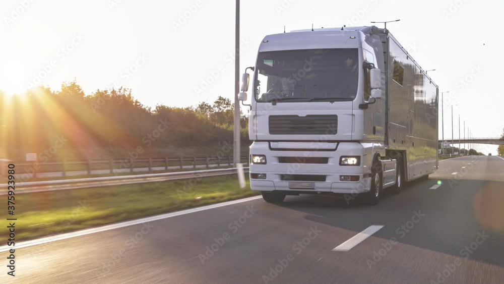 Cargo truck with cargo trailer driving on a highway. White Truck delivers goods in early hours of the Morning - very low angle drive thru close up shot. Cargo truck with cargo trailer driving on a highway. White Truck delivers goods in early hours of the Morning - very low angle drive thru close up shot.