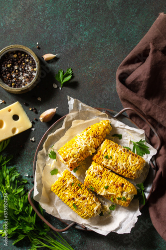 Summer vegan dinner or snacks. Grilled corn with garlic butter, served with cheese on a dark stone table top. Top view flat lay background. Copy space.