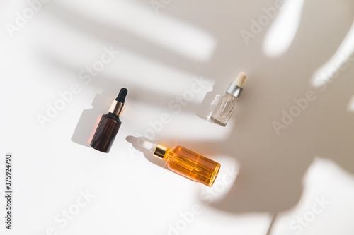 White, orange and black serum bottles on white background. Trending shadow from a palm branch. Cosmetic mockup. Place to insert text, images. Top view. Flat lay.