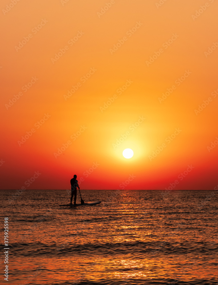 Man on the water paddle board at golden sunrise. vertical photo