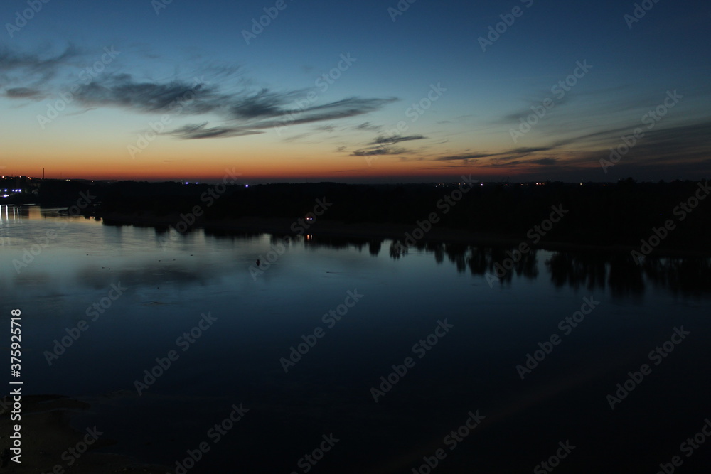 Sunset over the river blue and red sky stars and trees forest reflected on the water