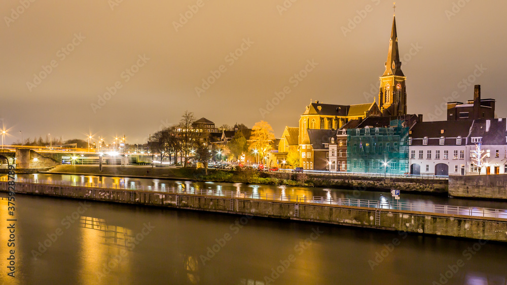 Obraz premium Night view of the river Maas (Meuse) with beautiful reflections of multicolored lights on a quiet December night in Maastricht, South Limburg in the Netherlands Holland