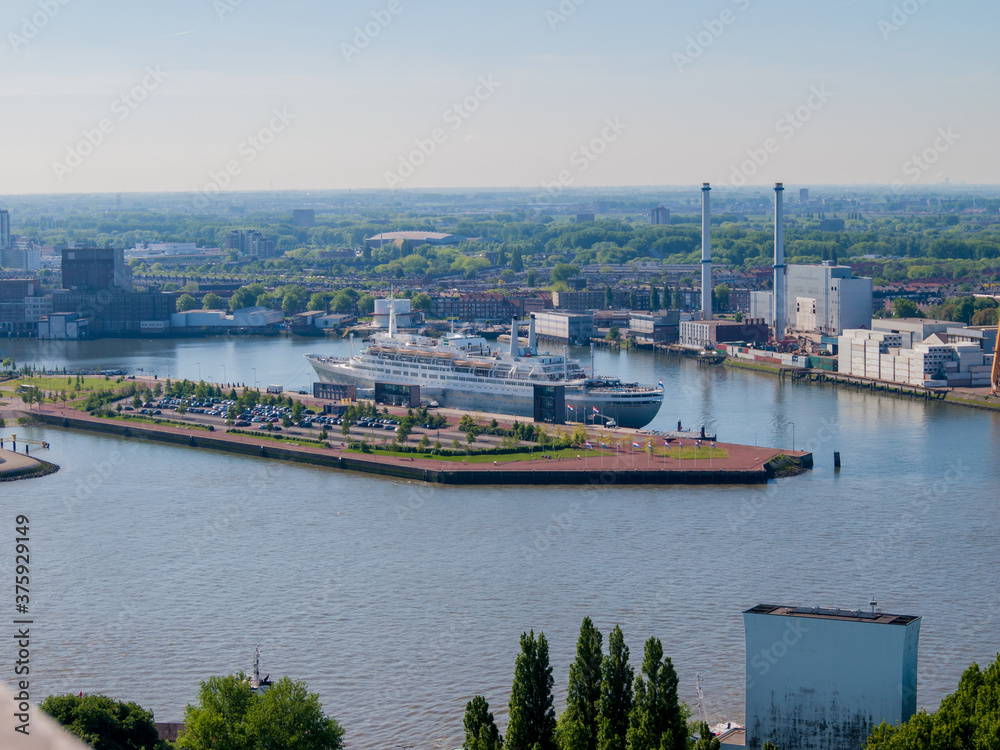 Aerial view of the Maas (Meuse) river with a cruise hotel anchored in the quay of the port of the city of Rotterdam with an urban landscape in the background, cloudy and gray day in the Netherlands