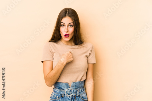 Young caucasian woman isolated en beige background surprised pointing with finger, smiling broadly.