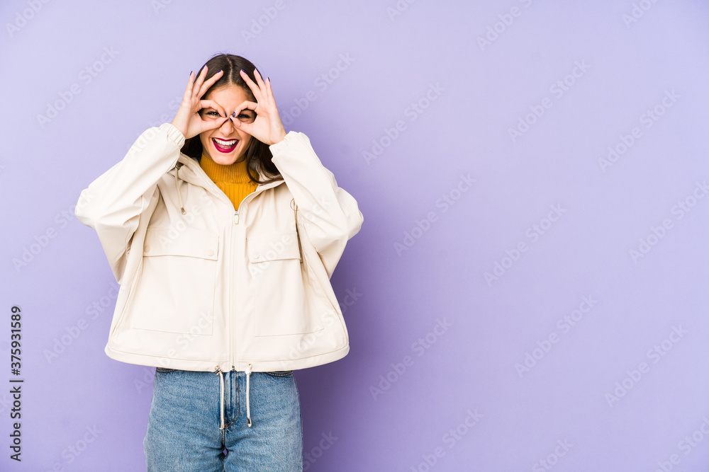 Young caucasian woman isolated on purple background showing okay sign over eyes Young caucasian woman isolated on purple background showing okay sign over eyes