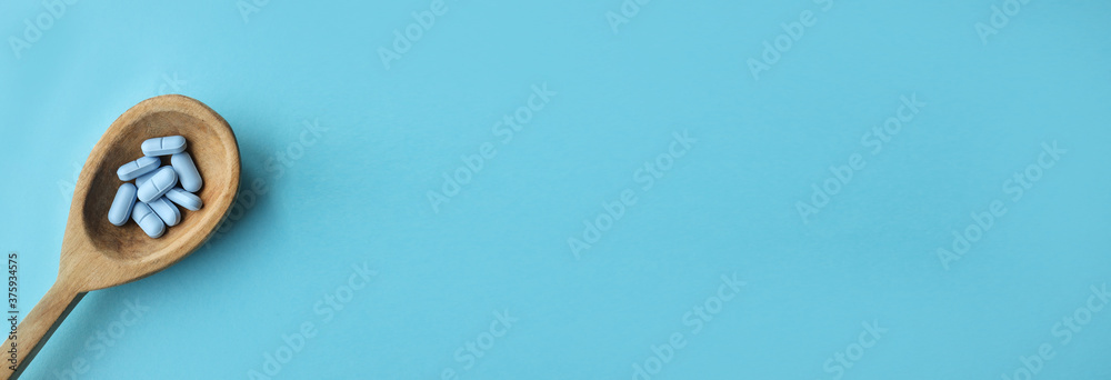 blue pills in a wooden spoon. blue background. drugs on a wooden spoon. Treatment of patients from the virus. Strengthening the immune system. Web Banner.Banner blue pills in a wooden spoon. blue background. drugs on a wooden spoon. Treatment of patients from the virus. Strengthening the immune system. Web Banner.Banner