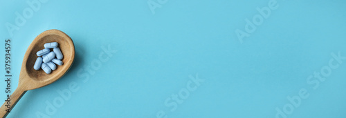 blue pills in a wooden spoon. blue background. drugs on a wooden spoon. Treatment of patients from the virus. Strengthening the immune system. Web Banner.Banner