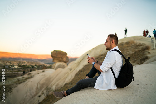 Man with cellphone and backpack sitting on rock