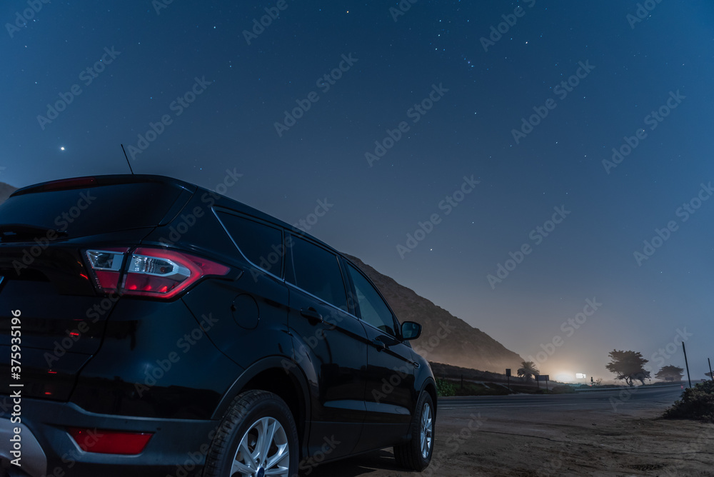 Naklejka premium Black compact car parked along highway as constellation Orion is overhead in the star lit night sky.