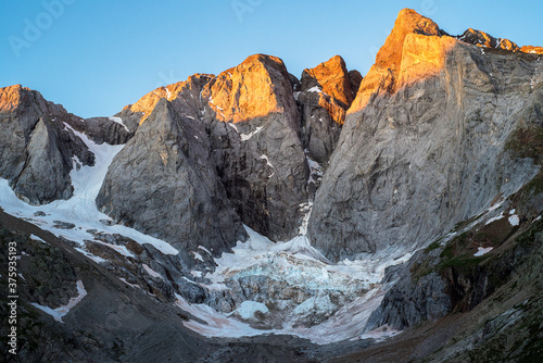 pics de montagne illuminés en jaune par le lever du soleil et glacier au dessous 