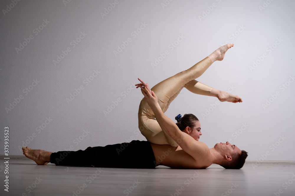 Obraz premium A duet of acrobats showing a pair trick. A woman in gymnastics overalls in a handstand over a shirtless man lies on his back. Very flexible circus performers.