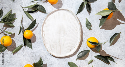 Whole oranges witl orange tree leaves on white background around empty plate. top view, flat lay, summer and healthy concept. Mockup photo