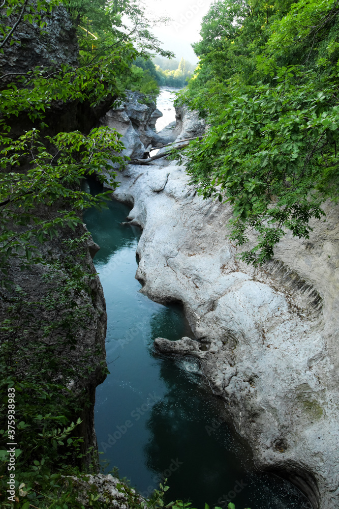 In the hollow, a blue river runs along the bottom. Mountain gorge, stone banks hang over the water of the mountain river.