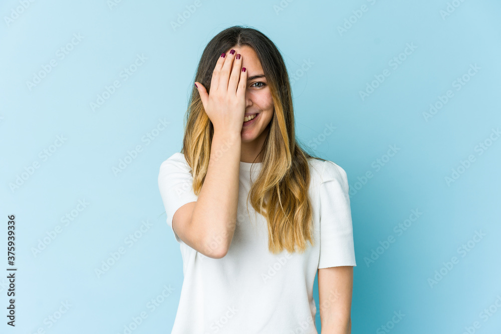 Young caucasian woman isolated on blue background having fun covering half of face with palm. Young caucasian woman isolated on blue background having fun covering half of face with palm.