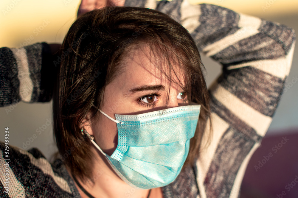 Young woman using surgical mask and looking far away during a sunset.