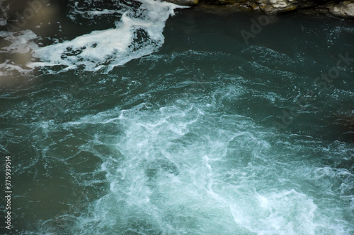 A mountain river runs among the stones. Water beats against stones and splashes fly in different directions.