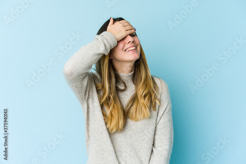Young caucasian woman isolated on blue background laughs joyfully keeping hands on head. Happiness concept.