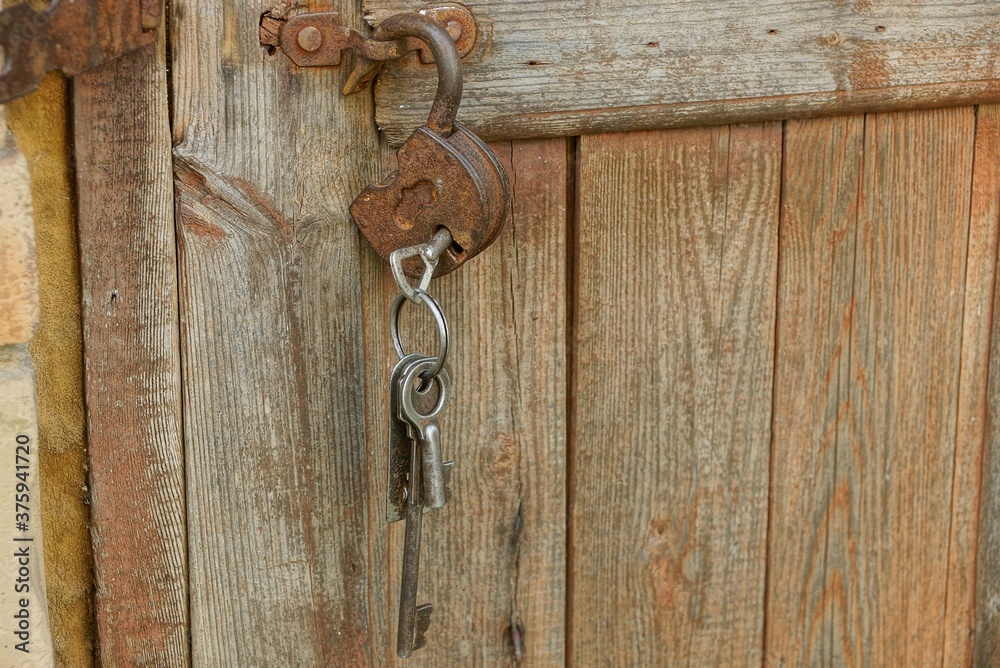 open brown iron rusty padlock with keys hanging on wooden planks door in the street