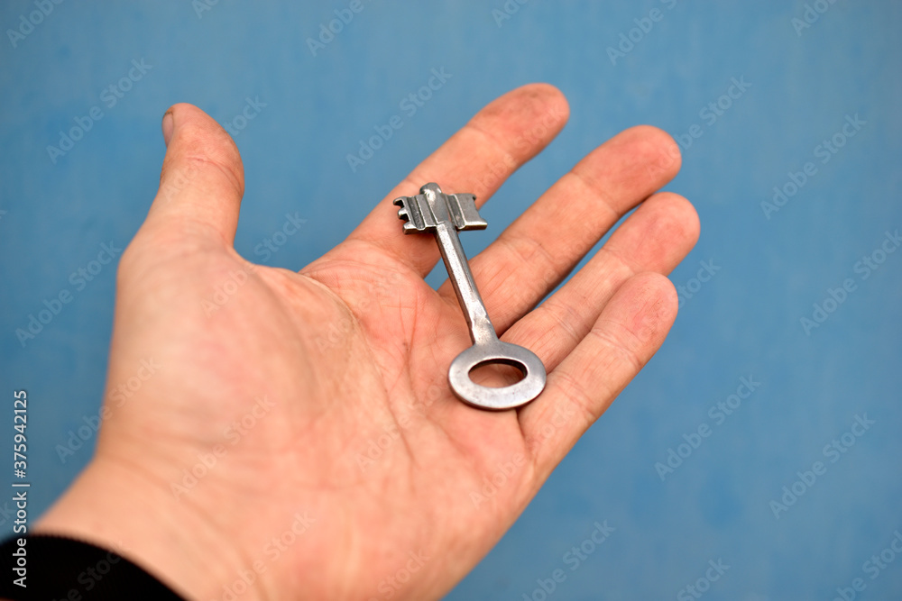 Old iron door key in hand on blue background
