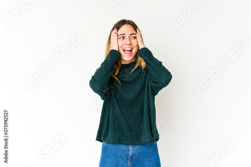 Young caucasian woman isolated on white background covering ears with hands trying not to hear too loud sound. © Asier