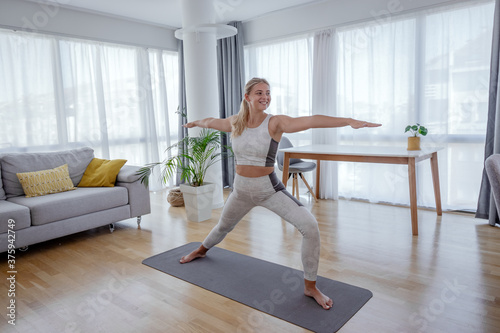 Beautiful active young woman making yoga asana Virabhadrasana warrior 2 pose at home. Healthy lifestyle and sports concept. Series of exercise poses.