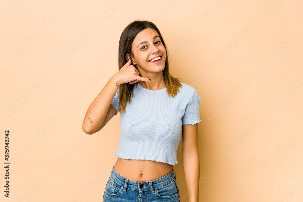 Young woman isolated on beige background showing a mobile phone call gesture with fingers. Young woman isolated on beige background showing a mobile phone call gesture with fingers.
