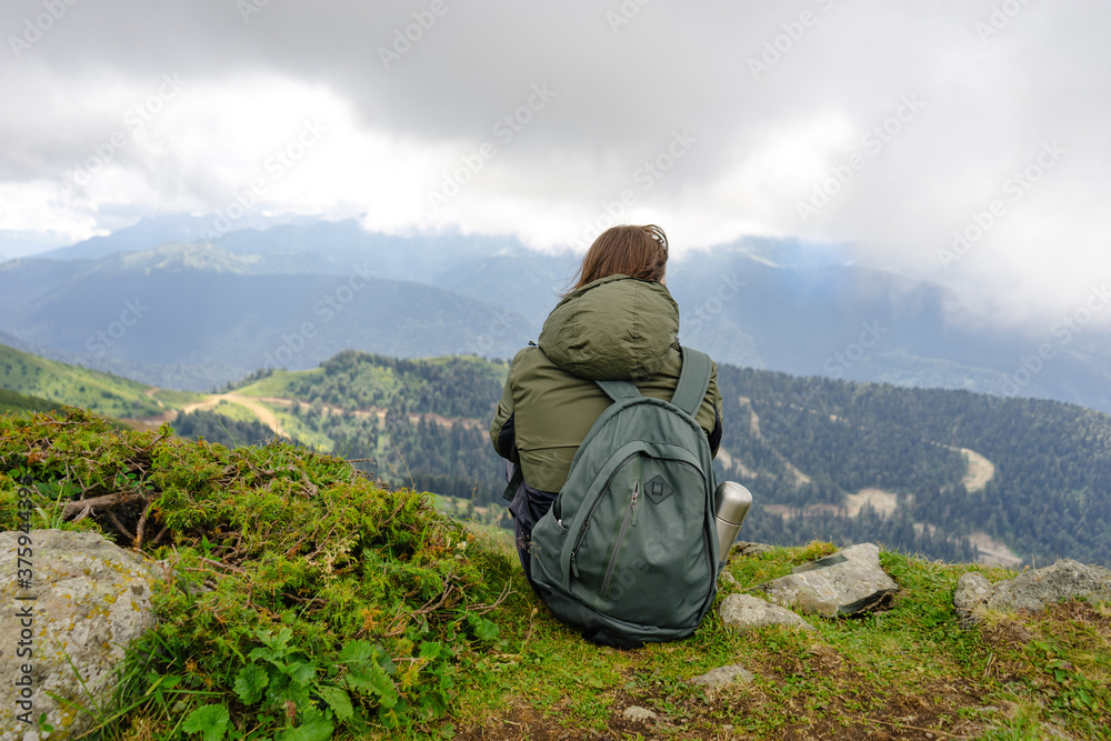 Young man sit in beautiful mountains on hiking trip. Active person resting outdoors in  nature. Backpacker camping outside recreation active