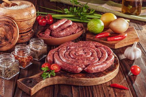 Raw thin brazilian sausages on the wooden board with ingredients - Linguiça toscaninha photo