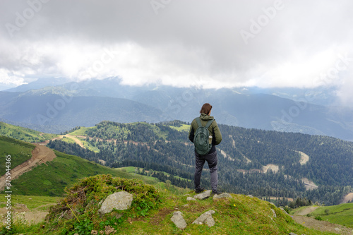 Young man hiker stand in beautiful mountains on hiking trip. Active tourist resting outdoors in nature. Backpacker camping outside recreation active