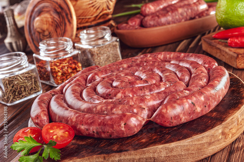 Raw thin brazilian sausages on the wooden board with ingredients - Linguiça toscaninha