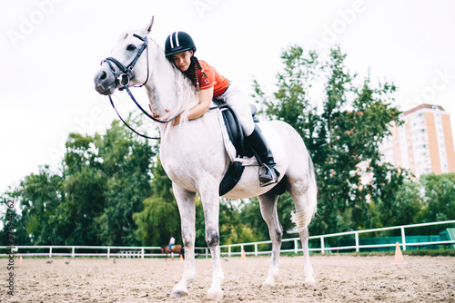 Young female jockey resting on horse while training