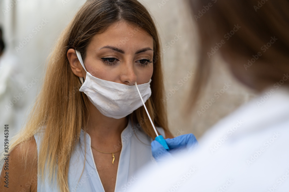 Doctor making a swab test to a young blonde woman for corona virus (covid-19) pandemic disease Doctor making a swab test to a young blonde woman for corona virus (covid-19) pandemic disease