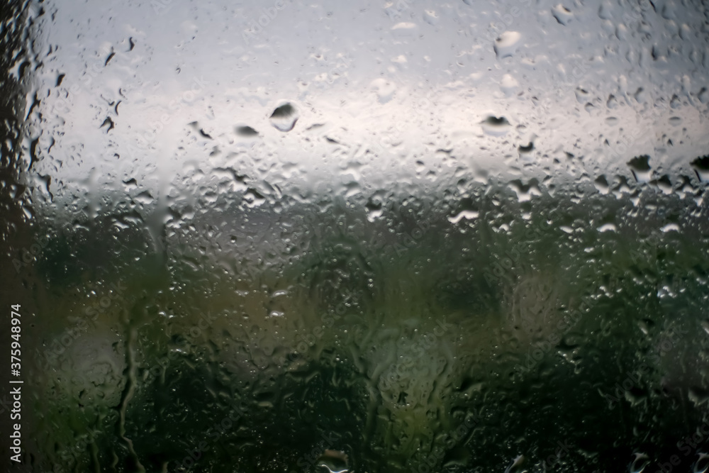 Raindrops on the window on a rainy gloomy day. Melancholy view through the wet glass of the gray sky, green dark trees outside. The concept of sadness, depression, and sadness Raindrops on the window on a rainy gloomy day. Melancholy view through the wet glass of the gray sky, green dark trees outside. The concept of sadness, depression, and sadness