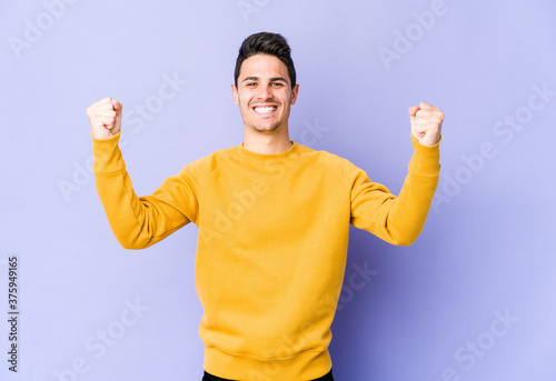 Young caucasian man isolated on purple background cheering carefree and excited. Victory concept.