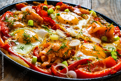 Shakshuka - fried eggs with salmon and vegetables in frying pan
