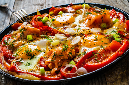 Shakshuka - fried eggs with salmon and vegetables in frying pan 