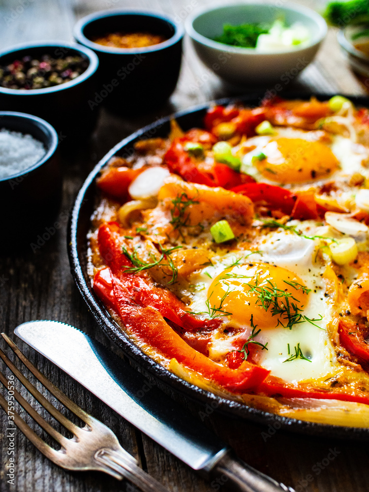 Shakshuka - fried eggs with salmon and vegetables in frying pan
