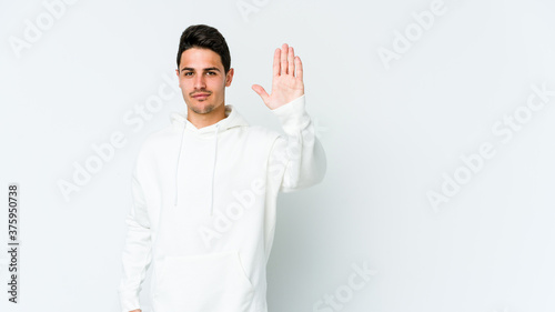 Young caucasian man isolated on white background standing with outstretched hand showing stop sign, preventing you. © Asier