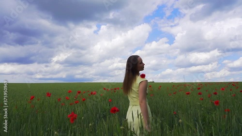 Beautiful young girl on a wheat green field with red poppies is dreaming, slow motion outdoors