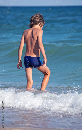 happy boy with his back walks into the sea with splashes and waves, vertical format
