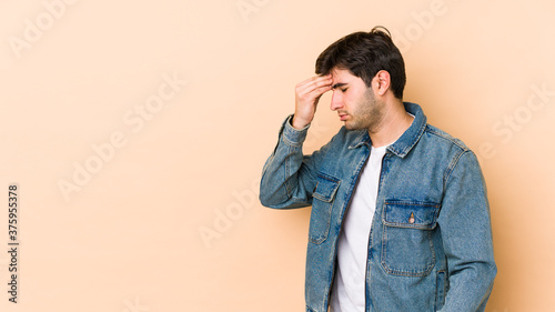 Young man isolated on beige background having a head ache, touching front of the face.