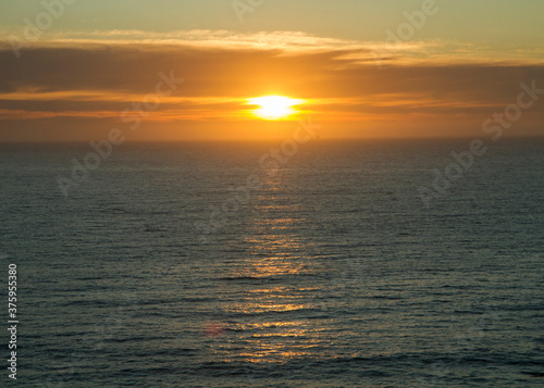 Heavens. Dramatic beach seascape. Beautiful sunset sky with orange sun rays and clouds, over the sea and ocean waves. The reflection of the sun in the pure water surface. 