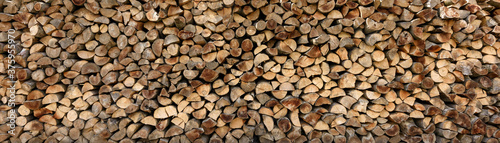 Wall of firewood, background of dry chopped firewood. Alternative fuel concept. Wide angle shot of natural background. Panoramic image in banner format.
