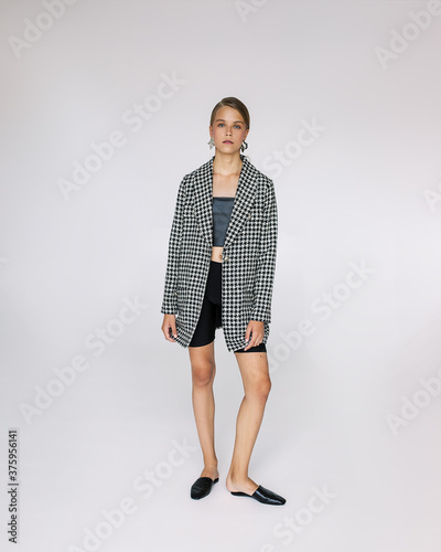 A young beautiful brown haired woman in a fashionable coat and shoes looking at the camera. Check. Large earrings in the ears. Fashion blogger, style concept. Full length photo