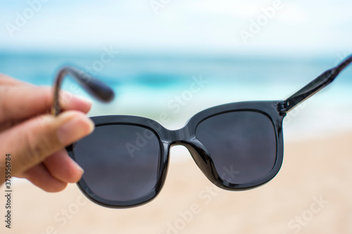 Hand wearing sunglasses on the beach with blurred sea beach background , selective focus