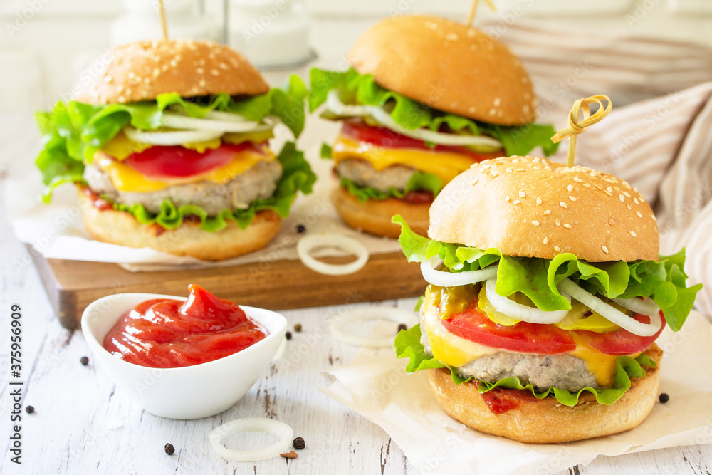 Delicious burgers, hamburger sandwich with cutlet, cheese, bacon and tomatoes on a wooden table.