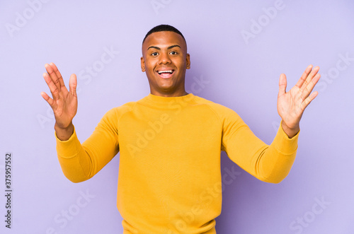Young latin man isolated on purple background receiving a pleasant surprise, excited and raising hands.